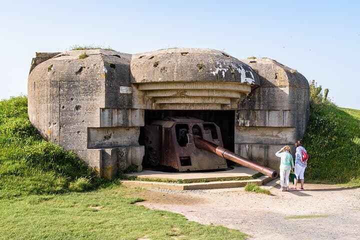 Two tourists observe the 150 mm gun in a bunker in the Longues-sur-Mer battery in Normandy, France, a WWII German coastal artillery battery part of the Atlantic Wall fortifications.