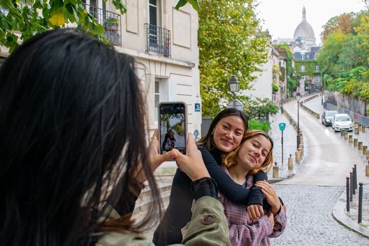 Girl with black hair taking a photo of 2 girls in front of a street